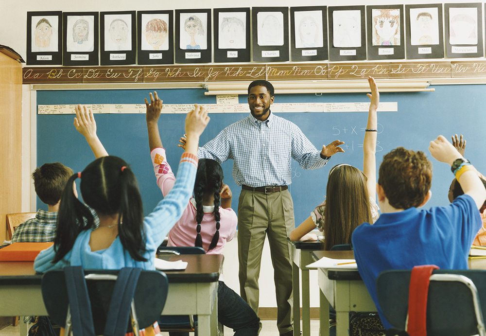 teacher in front of class of children with raised hands