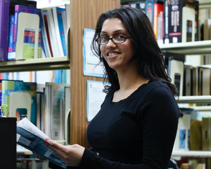 GSE student smiling in library while holding a book.